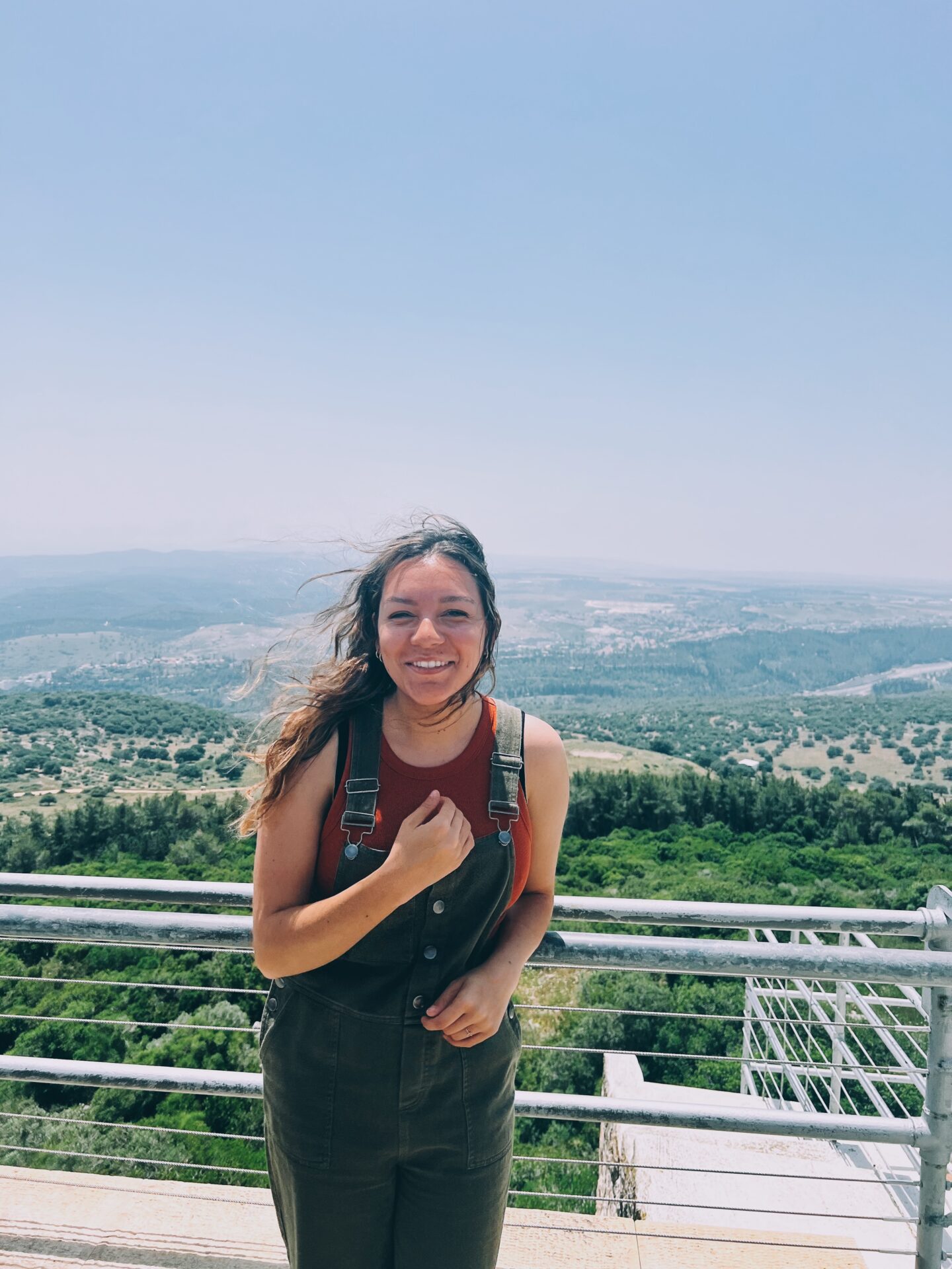 A smiling girl standing on top of Mountain Carmel with a mountainous view behind her. 