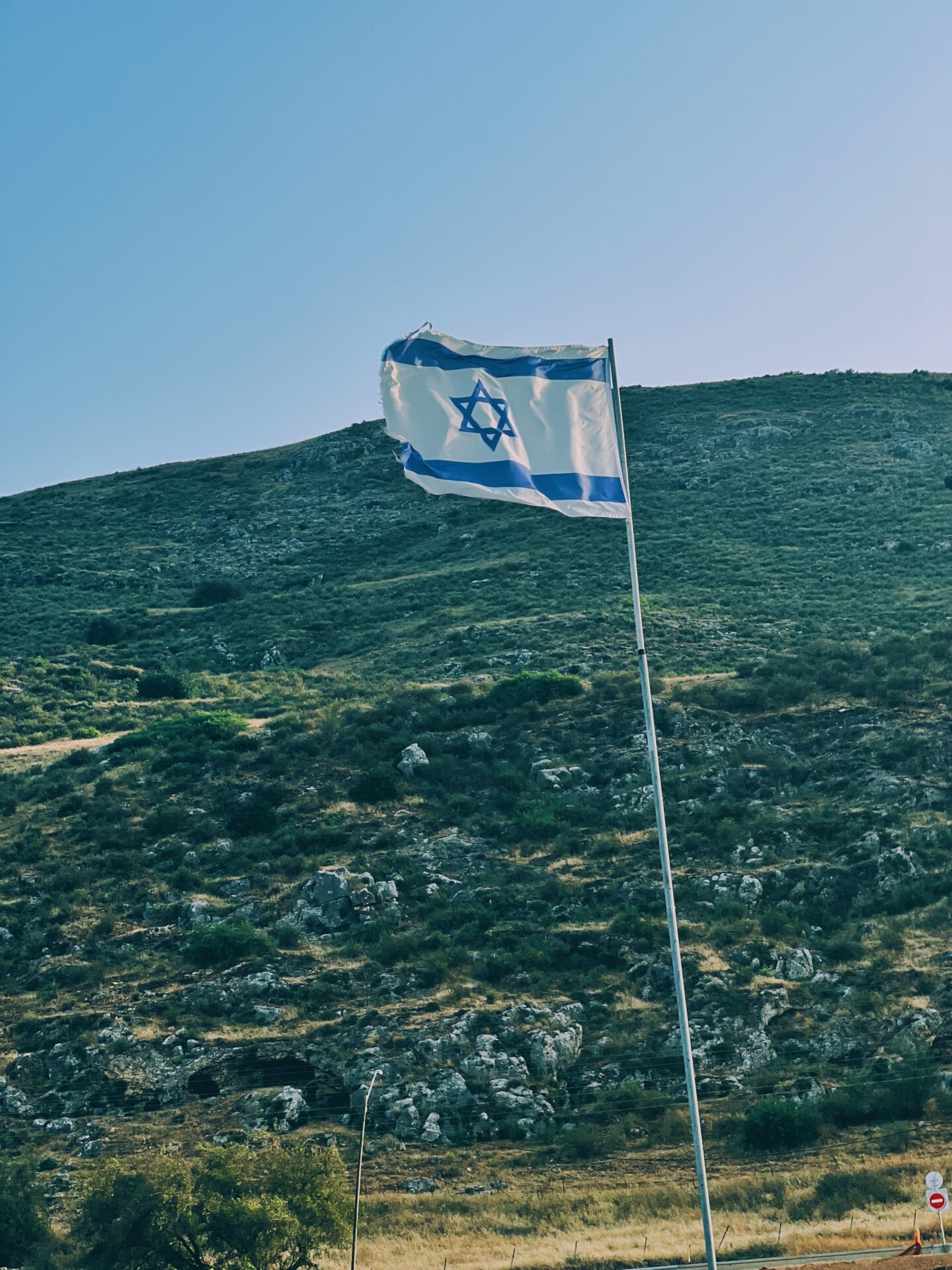 Israeli flag flying in front of a rocky hill.